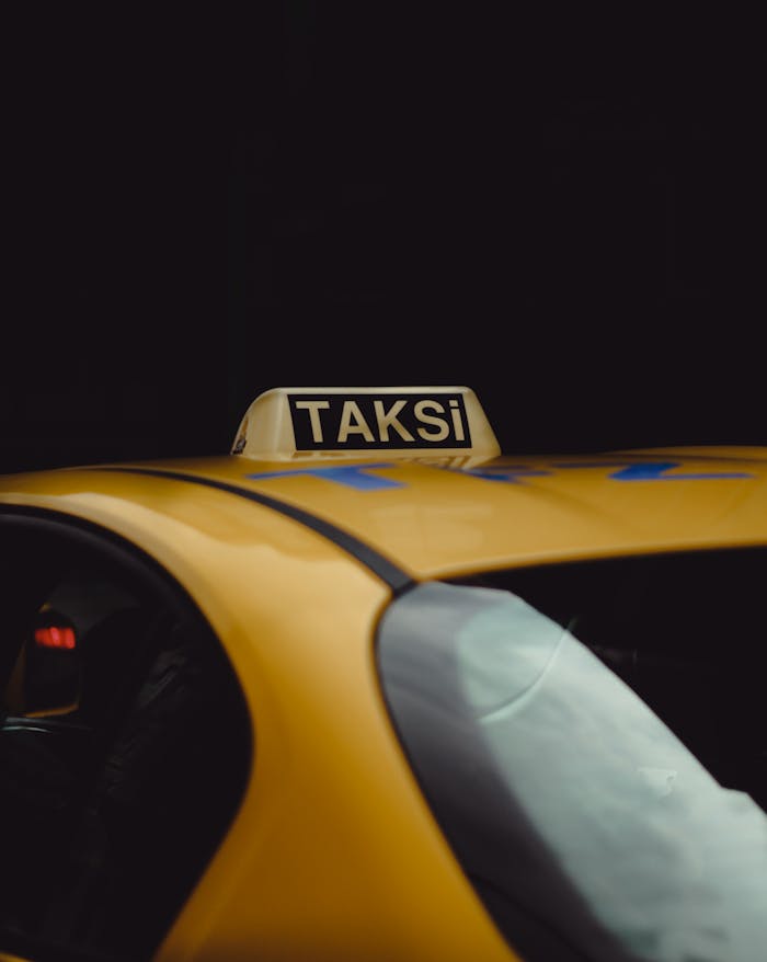 our-services-2 Close-up of a yellow taxi with a 'Taksi' sign, captured in an urban environment with a dark background.
