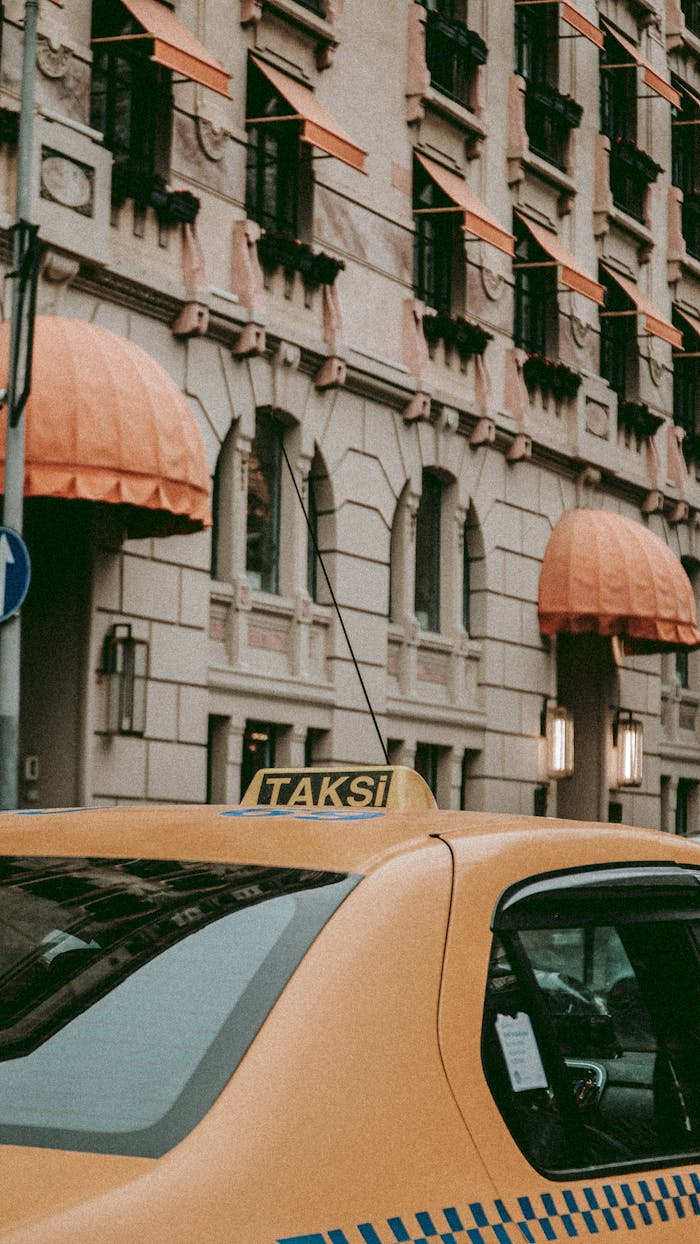 Yellow taxi in front of a building with classic architecture and orange awnings.
