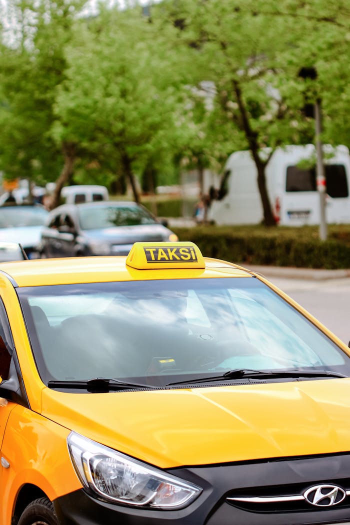A close-up view of a yellow taxi in a bustling urban street, surrounded by green foliage.