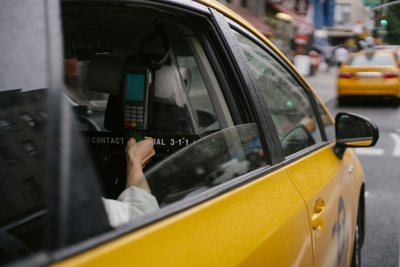 about-01 Close-up of passenger's hand using payment terminal inside a yellow taxi cab on a city street.